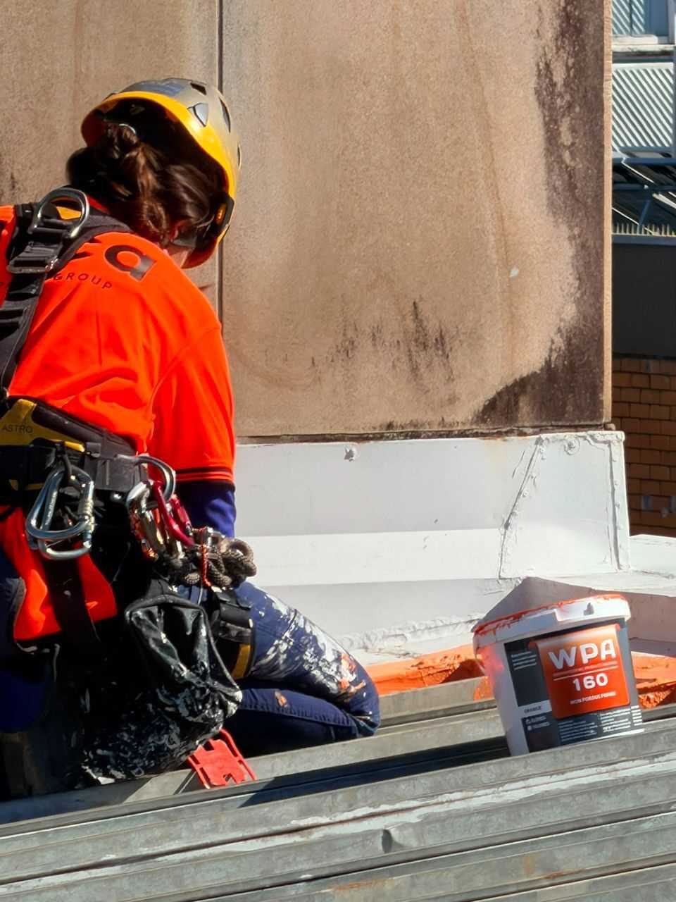 A Deca technician in rope access harness applying WPA160 primer at the parapet, 368 Ruthven Street